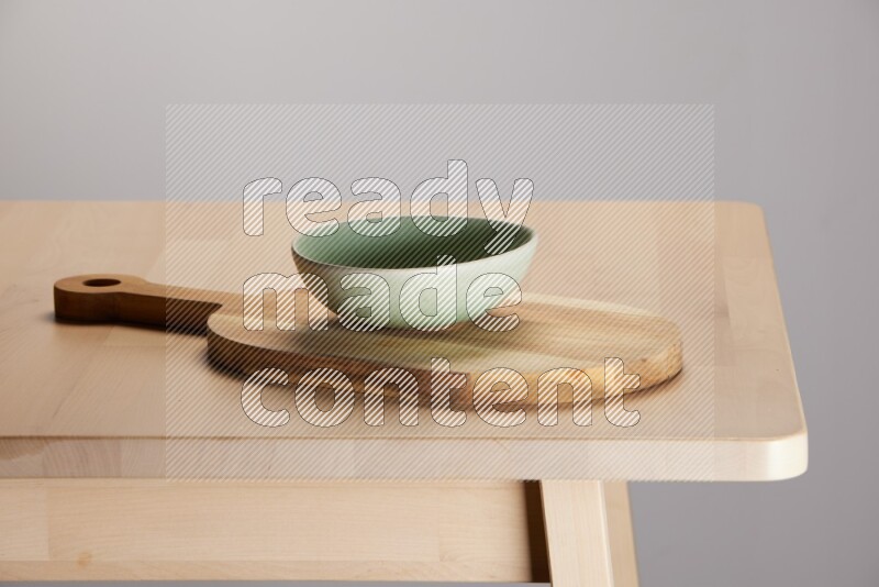 green bowl placed on a  wooden oval cutting board on the edge of wooden table