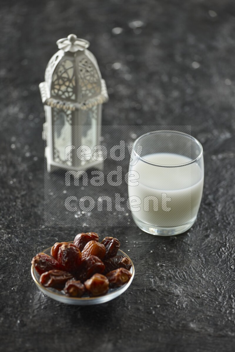A white lantern with different drinks, dates, nuts, prayer beads and quran on textured black background