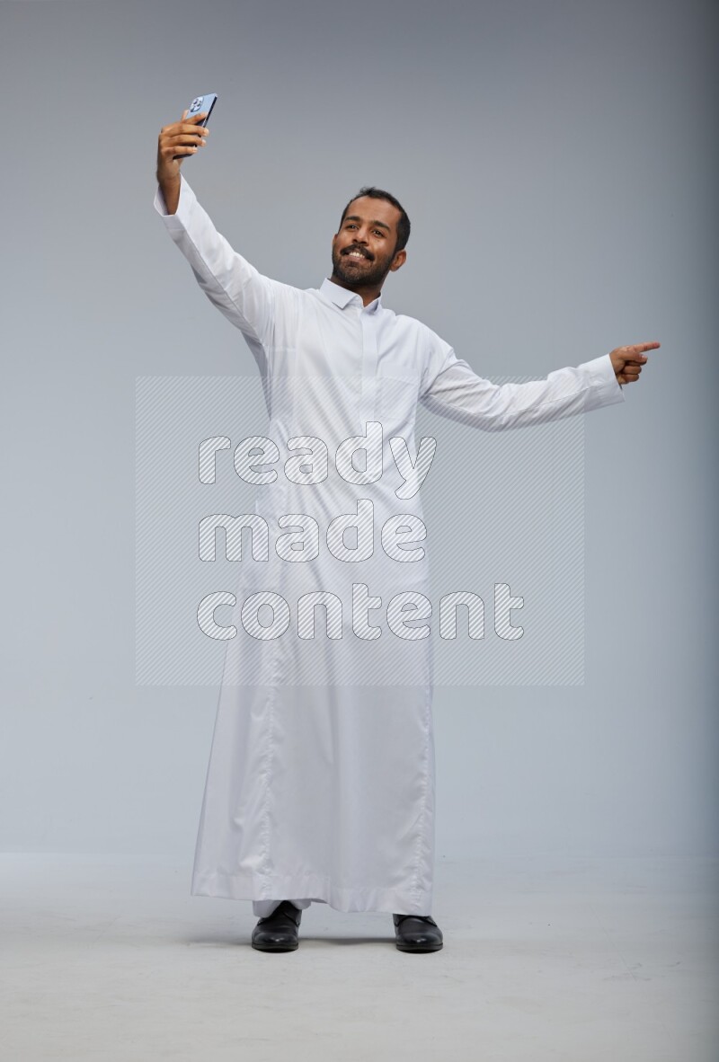 Saudi man wearing Thob standing taking selfie on Gray background