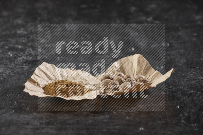 قطعتان من الورق المجعد ممتلئتان بحبوب وبودرة جوزة الطيب علي خلفية سوداء