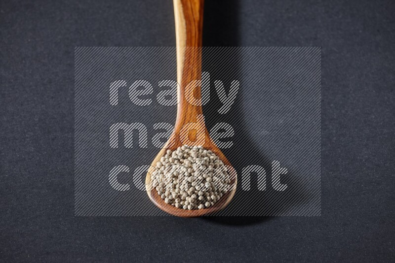 A wooden ladle full of white pepper beads on black flooring