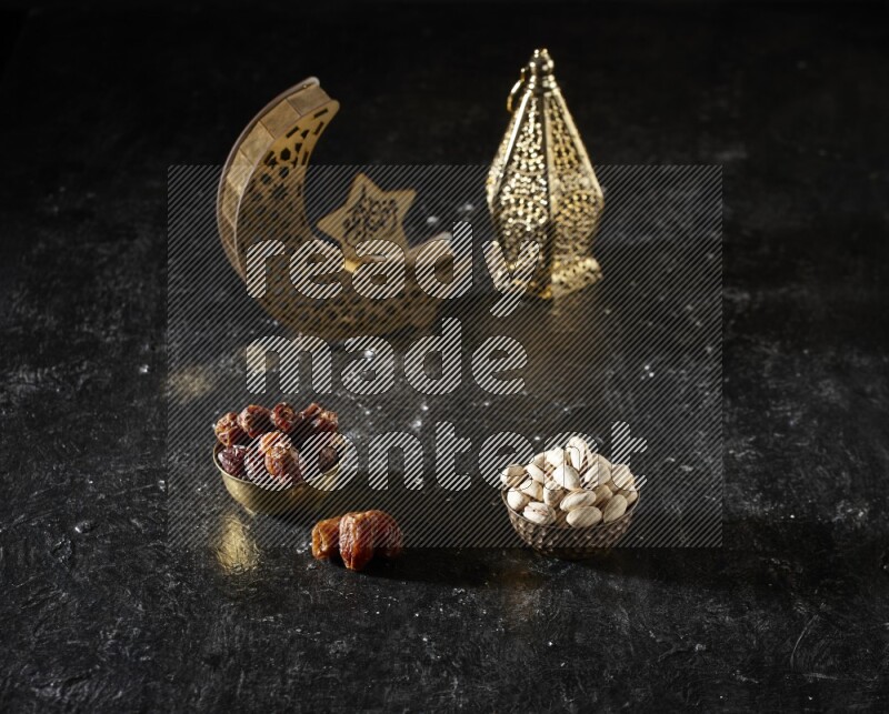 Dates in a metal bowl with pistachios beside golden lanterns in a dark setup