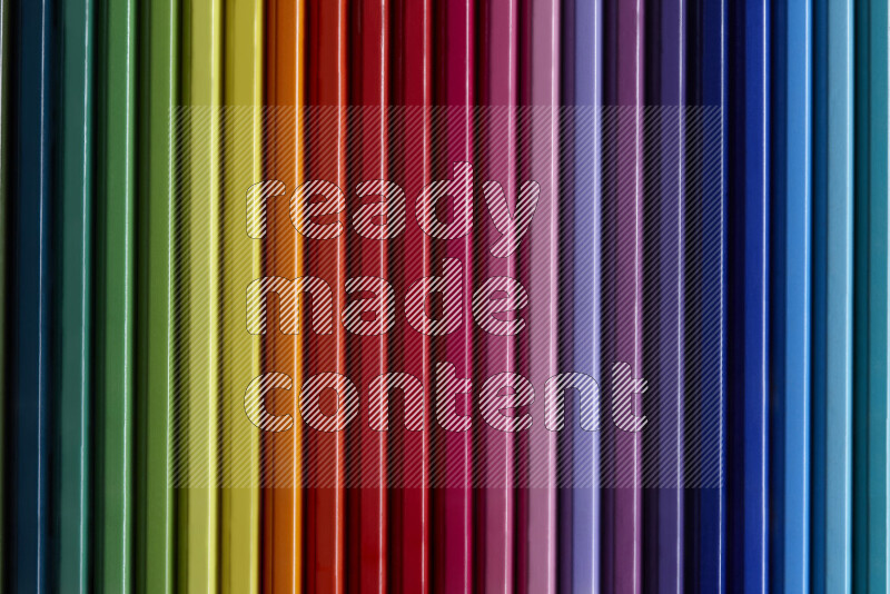 A collection of colored pencils arranged showcasing a gradient of different hues on grey background