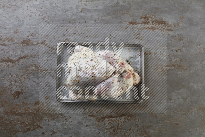 whole Raw chicken on a small oven trey direct on a rustic grey background