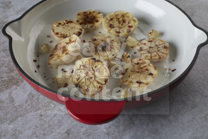 half's roasted garlic in a red-coated cast iron pan on a grey textured countertop