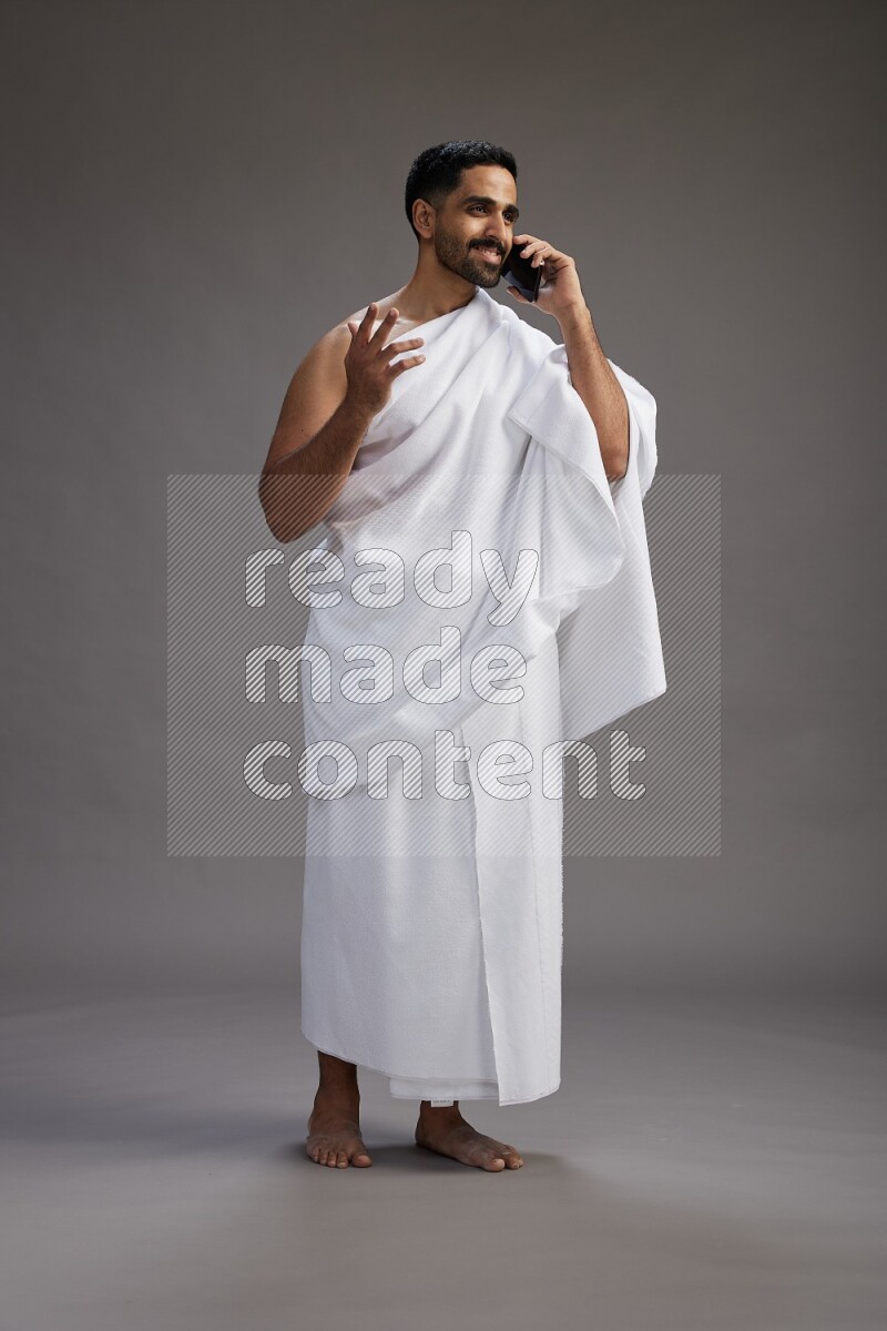 A man wearing Ehram Standing talking on phone on gray background