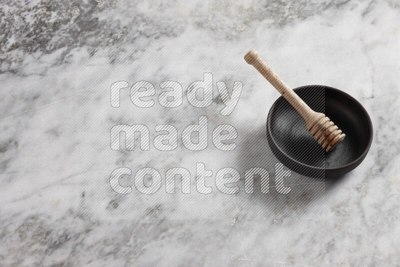 Black pottery bowl with wooden honey dipper in it on grey marble background