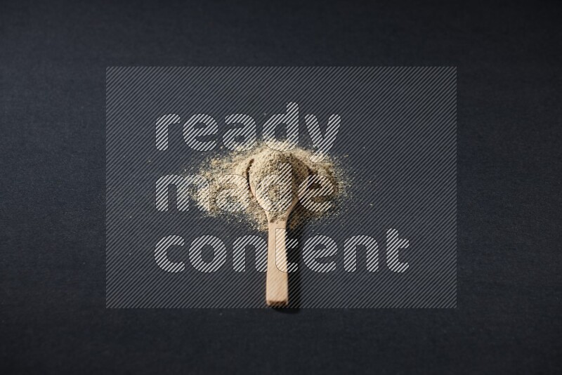 A wooden spoon full of cardamom powder and powder spreaded on black flooring