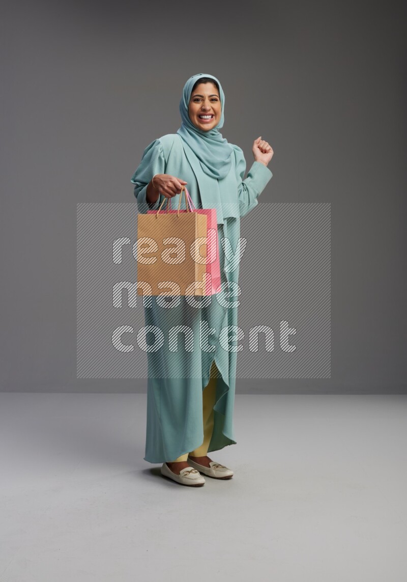 Saudi Woman wearing Abaya standing holding shopping bag on Gray background