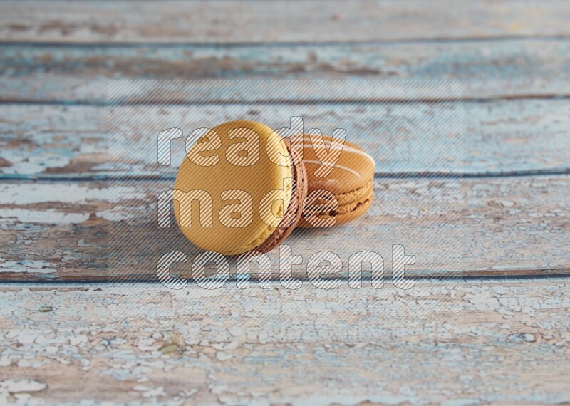 45º Shot of of two assorted Brown Irish Cream, and Yellow, and Brown Chai Latte macarons  on light blue background