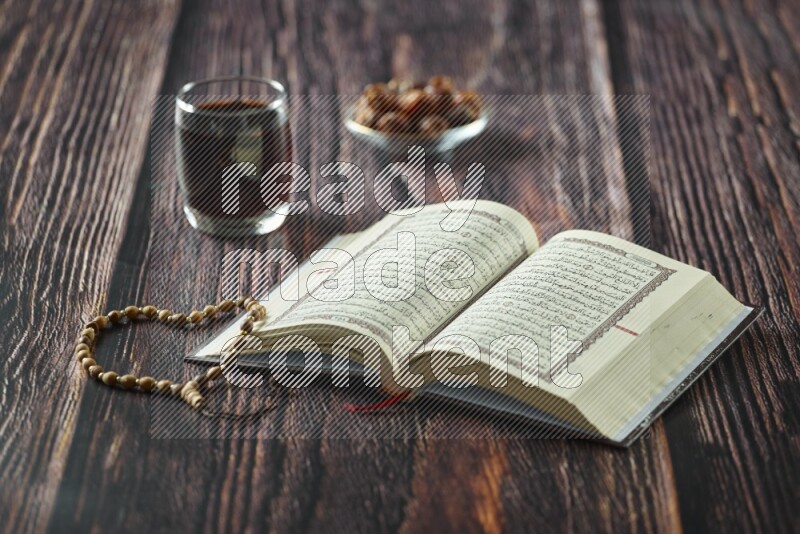 Quran with dates, prayer beads and different drinks all placed on wooden background