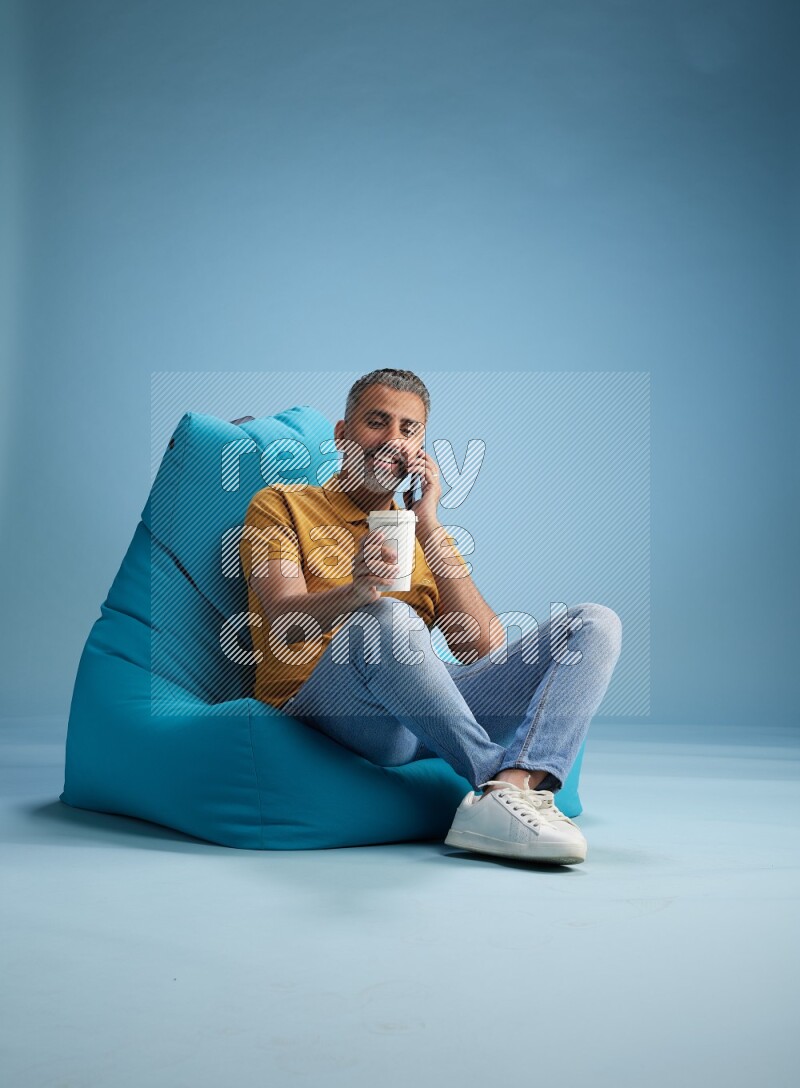 A man sitting on a blue beanbag and drinking coffee
