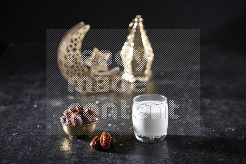 Dates in a metal bowl with milk beside golden lanterns in a dark setup