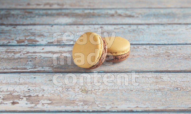 45º Shot of two Yellow and Brown Chai Latte macarons on light blue wooden background