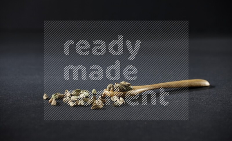 ملعقة خشبية ممتلئة بالهيل على خلفية سوداء