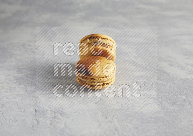 45º Shot of two Yellow Crème Brulée macarons on white  marble background