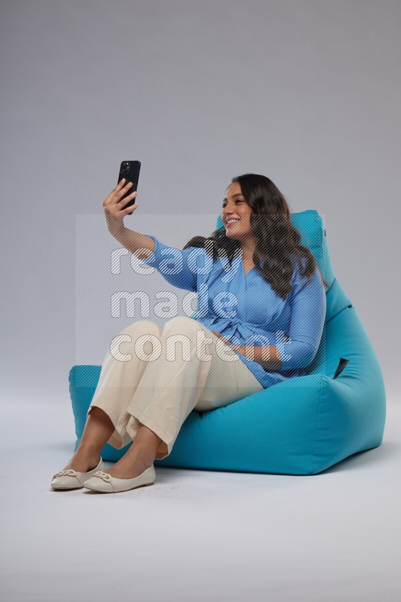 A woman sitting on a blue beanbag and taking selfie