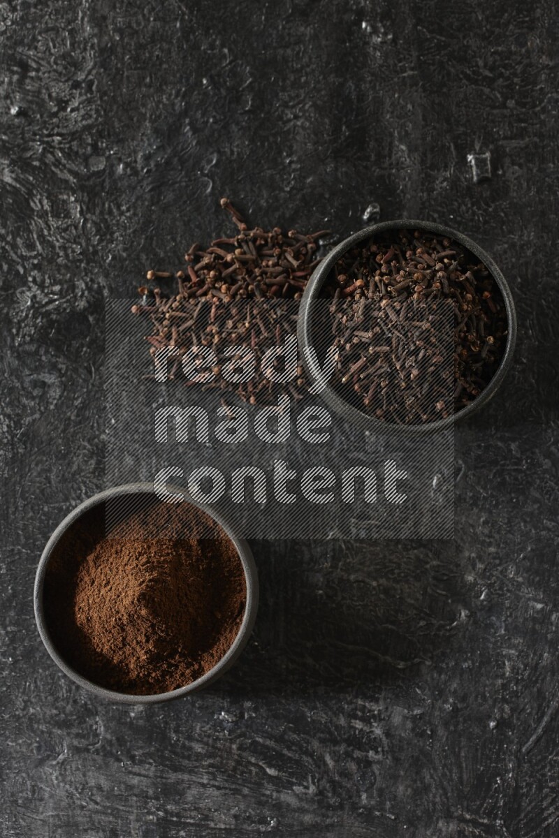 وعاءين من الفخار الأسود أحدهما ممتلئي بحبوب القرنفل والآخر ممتلئ ببودرة القرنفل على خلفية سوداء