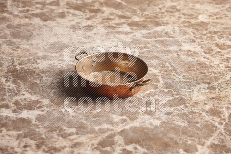 A small copper pan on beige marble background
