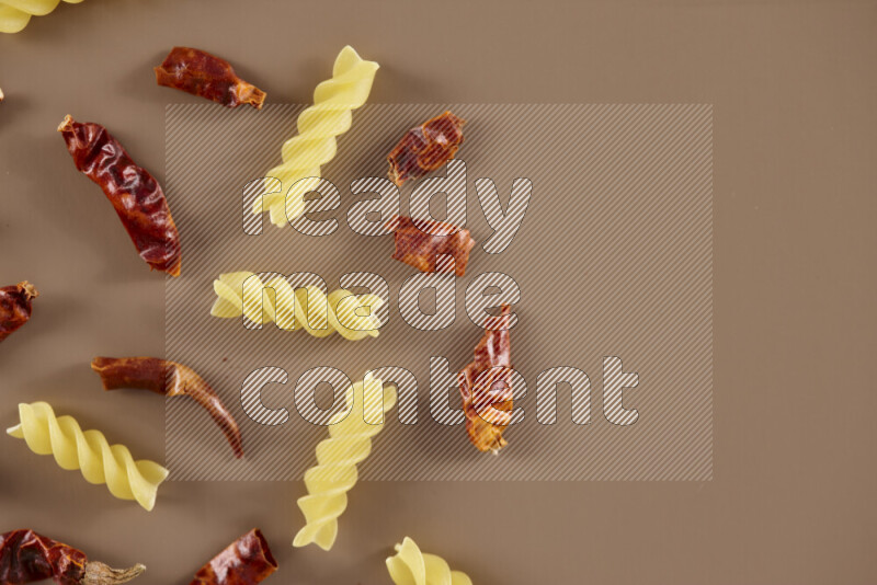 Raw pasta with different ingredients such as cherry tomatoes, garlic, onions, red chilis, black pepper, white pepper, bay laurel leaves, rosemary and cardamom on beige background