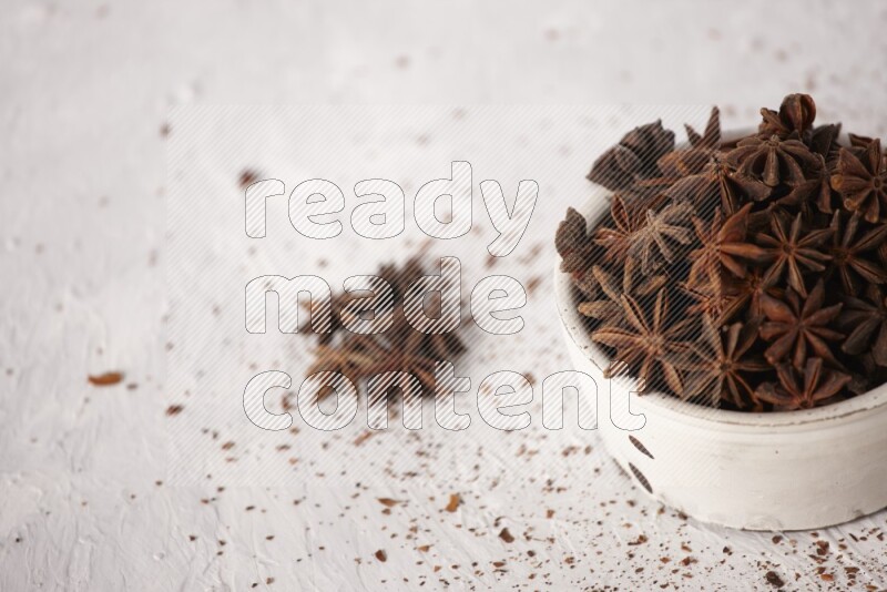 Star Anise in a white bowl and more of it sprinkled on white background