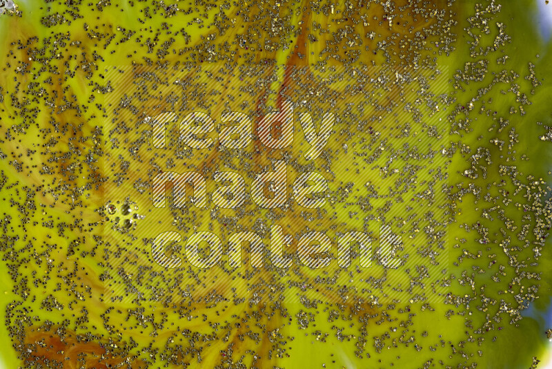 A close-up of sparkling gold glitter scattered on swirling green and red background