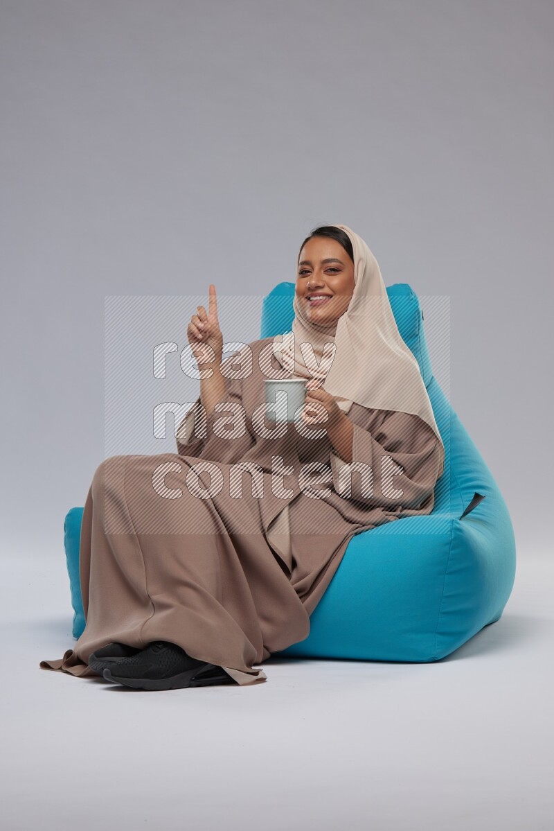 A Saudi woman sitting on a blue beanbag and drinking coffee