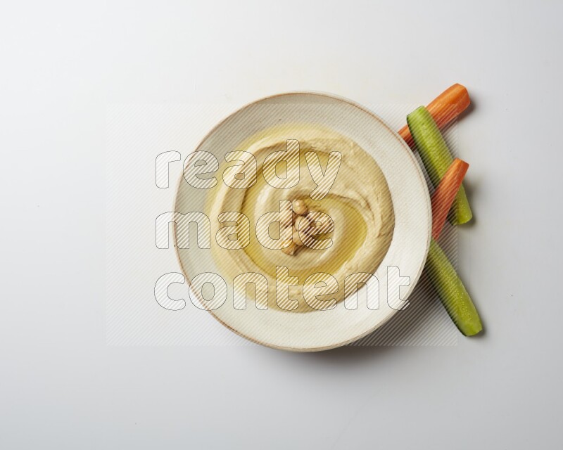 Hummus in a pottry plate garnished with roasted chickpeas on a white background