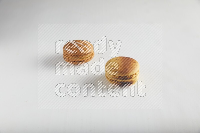 45º Shot of of two assorted Brown Irish Cream, and Yellow Crème Brulée macarons on white background