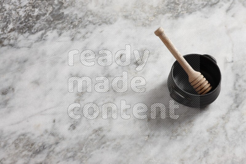 Black pottery bowl with wooden honey dipper in it on grey marble background
