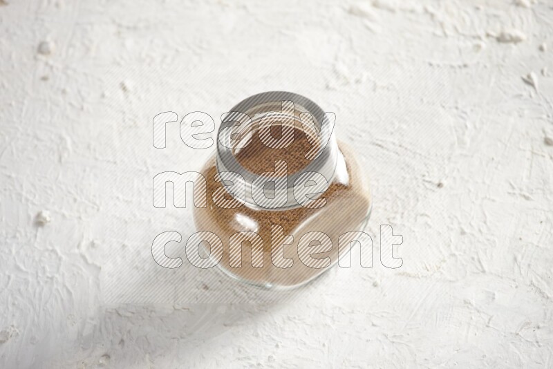 Herbs glass jar full of cinnamon powder on a textured white background