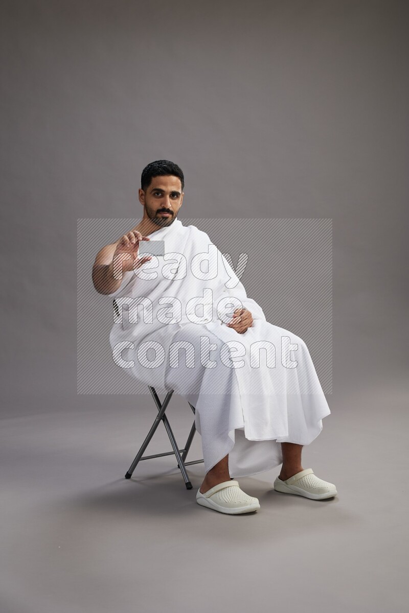 A man wearing Ehram sitting on chair holding ATM card on gray background