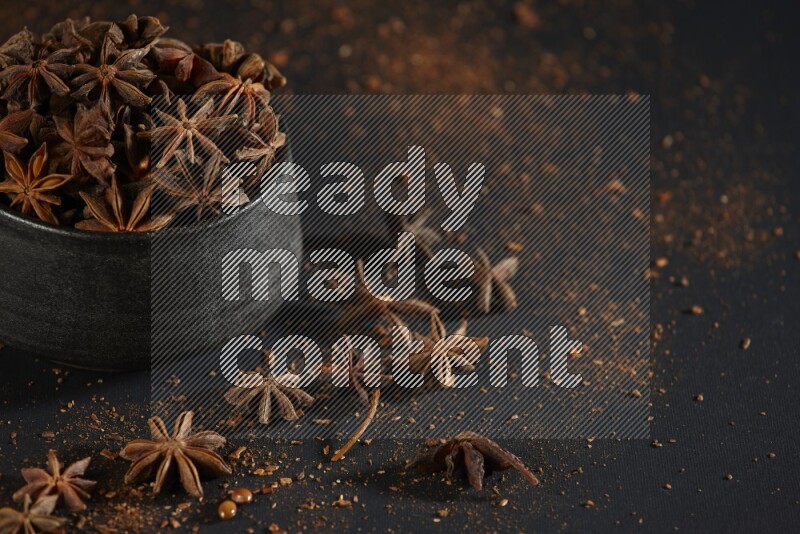Star Anise in a black bowl with sprinkled anise on black flooring
