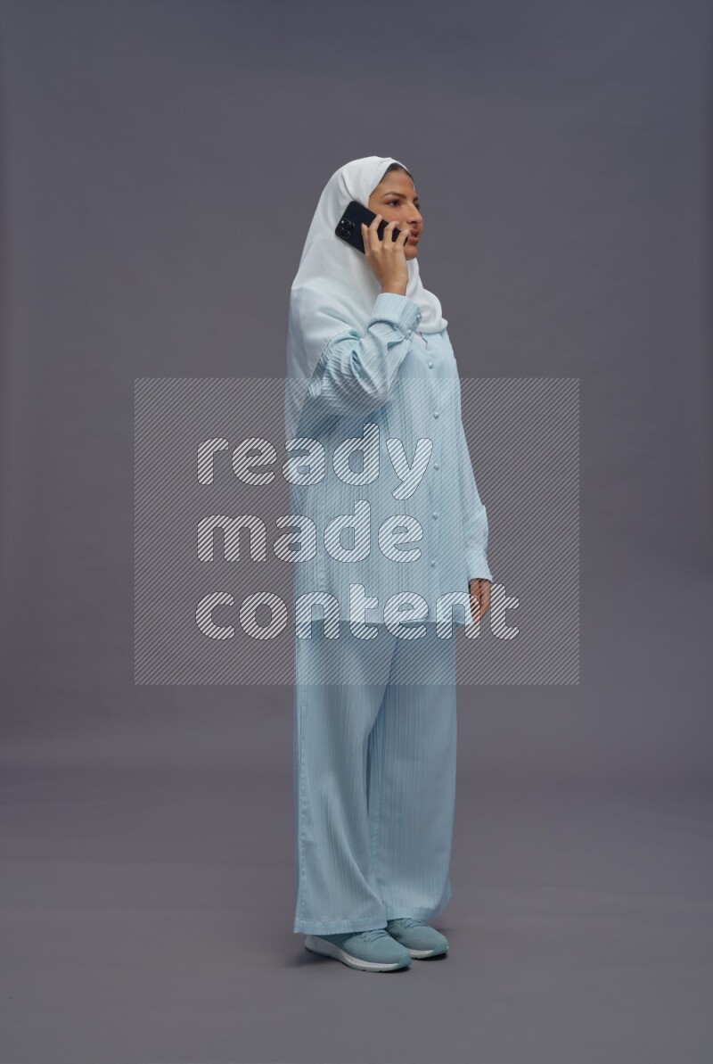 Saudi woman wearing hijab clothes standing talking on phone on gray background