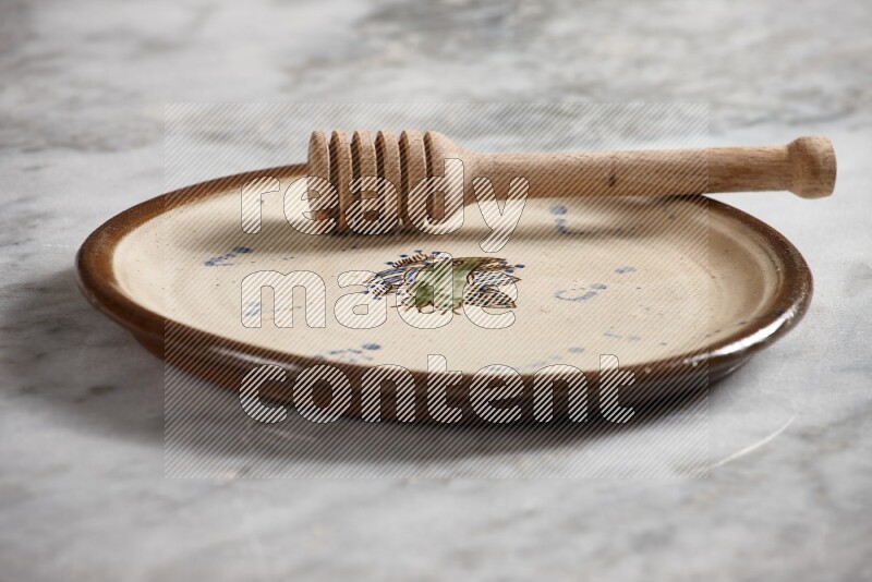Decorative pottery plate with wooden honey dipper in it on grey marble background