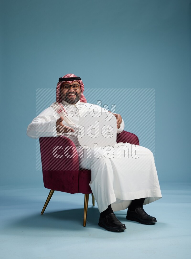 Saudi Man with shimag sitting on chair holding social media sign on blue background