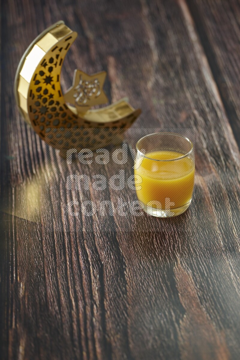 A wooden golden crescent lantern with different drinks, dates, nuts, prayer beads and quran on brown wooden background