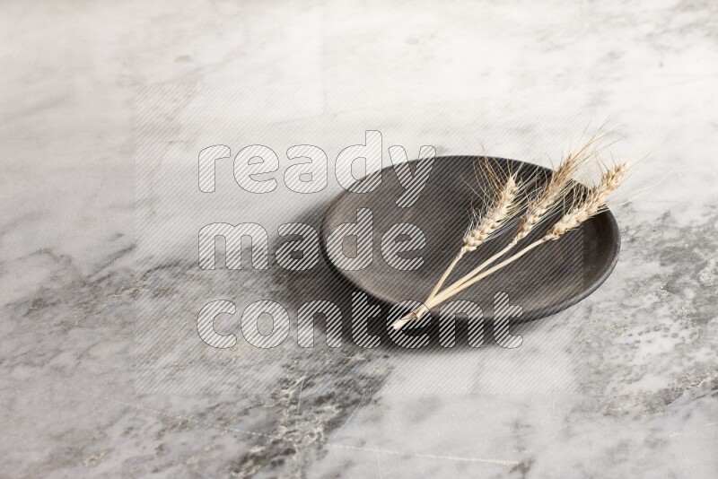 Wheat stalks on black pottery plate on grey marble background