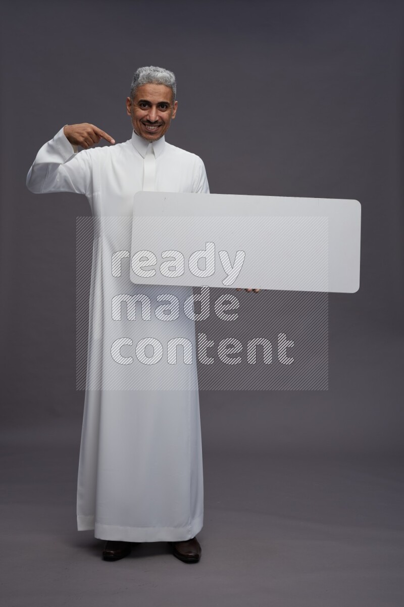 Saudi man wearing thob standing holding board on gray background