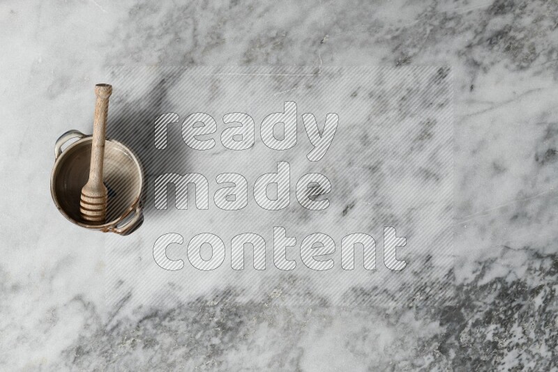 Multicolored pottery bowl with wooden honey dipper in it on grey marble background