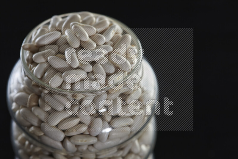 White beans in a glass jar on black background