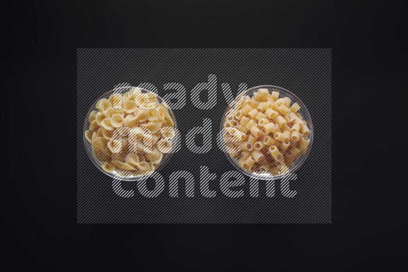 Different pasta types in glass bowls on black background