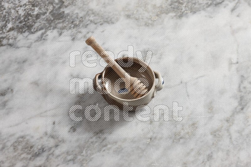 Multicolored pottery bowl with wooden honey dipper in it on grey marble background