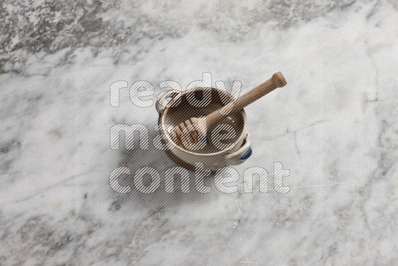 Multicolored pottery bowl with wooden honey dipper in it on grey marble background