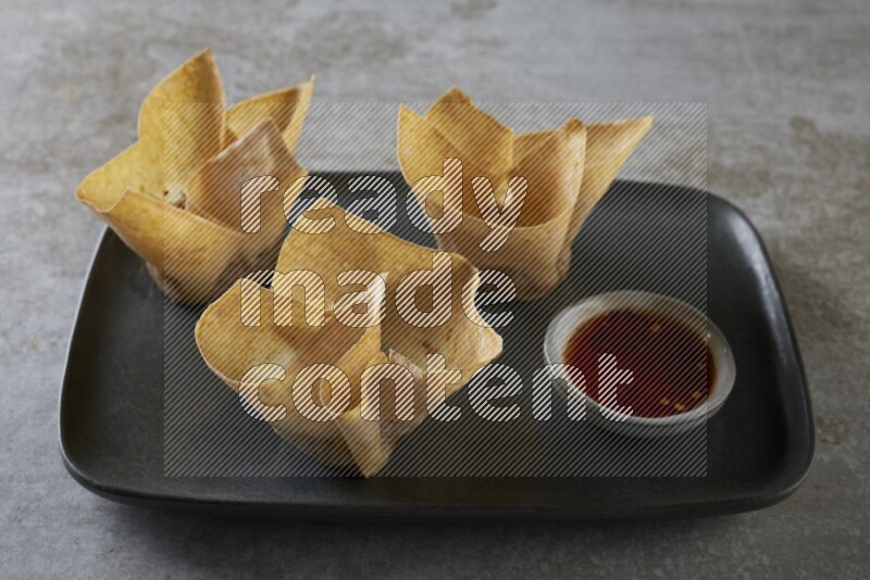 wonton cups with soy sauce ramkin on rectangle dark grey ceramic plate on grey textured counter top