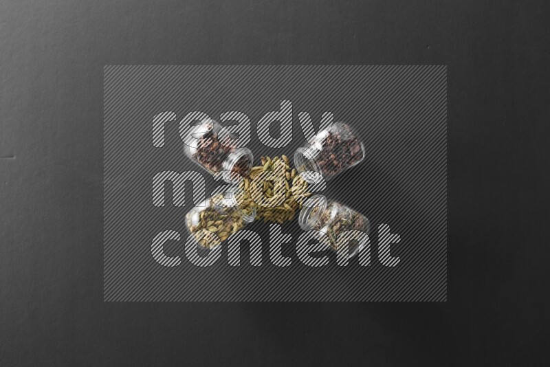 قرنفل وحبوب الهيل وريحان مجفف ويانسون نجمي في أوعية زجاجية علي خلفية سوداء