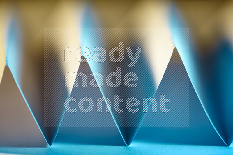 A close-up abstract image showing sharp geometric paper folds in blue gradients and warm tones