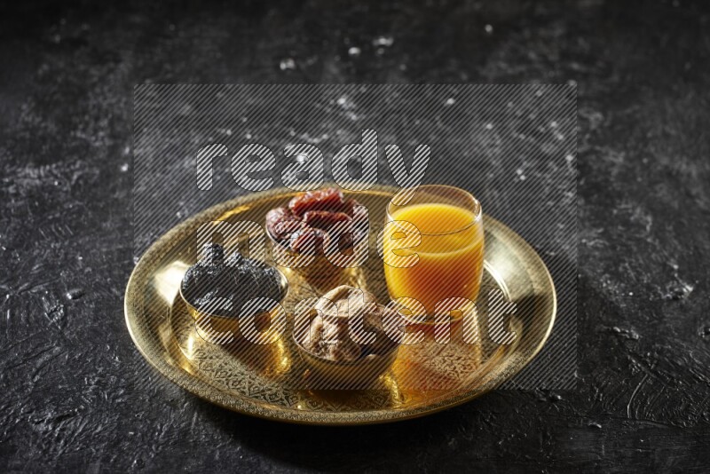 Dried fruits in metal bowls with qamar eldin on a tray in dark setup
