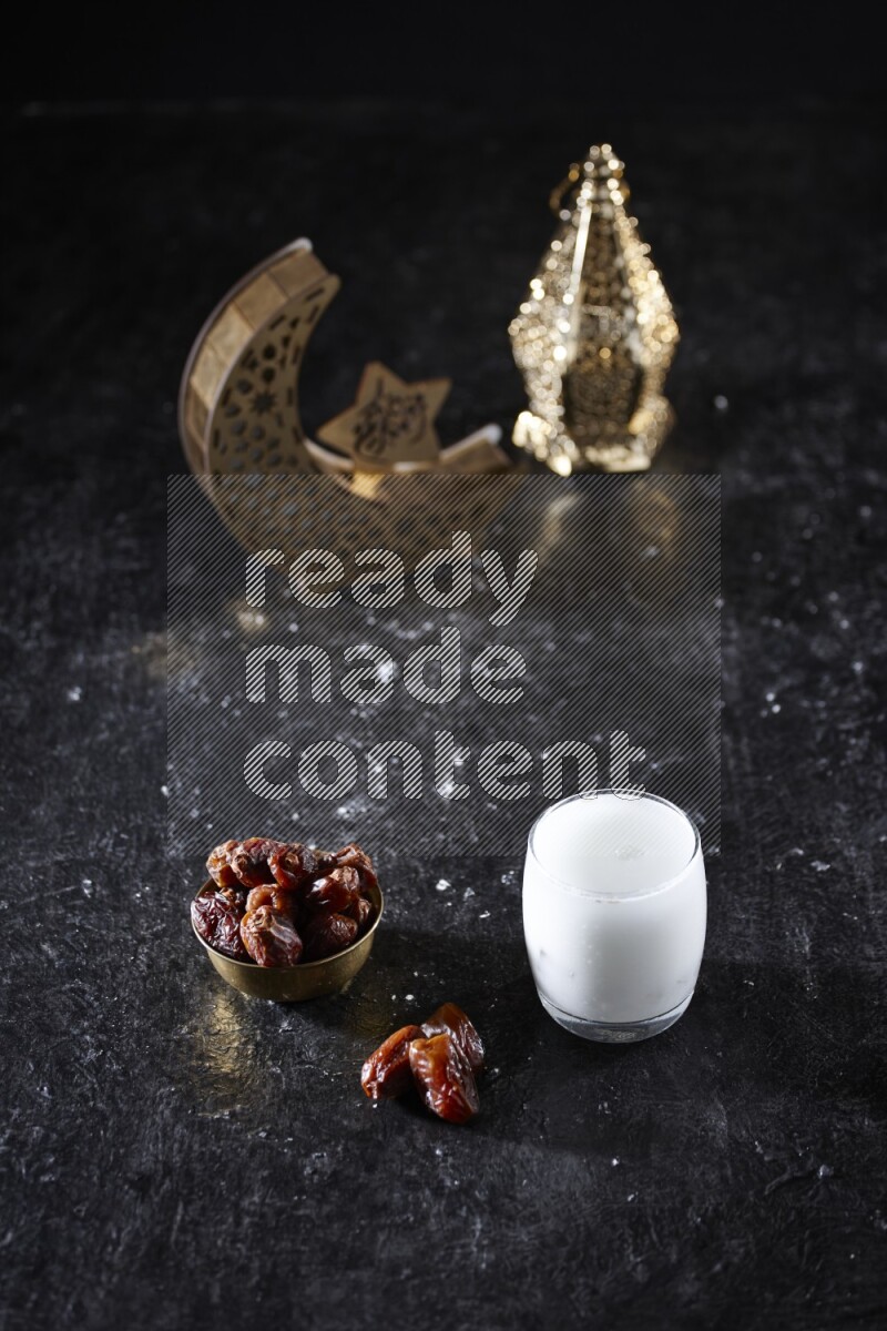 Dates in a metal bowl with sobia beside golden lanterns in a dark setup