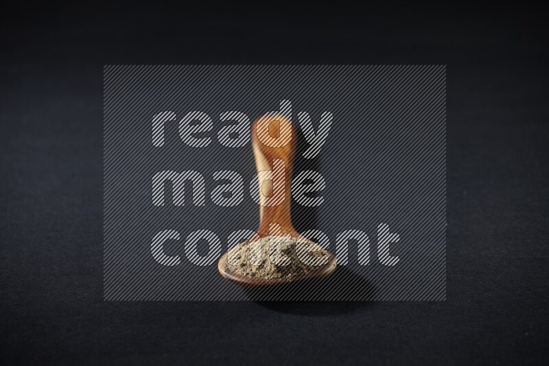 A wooden ladle full of cardamom powder on black flooring